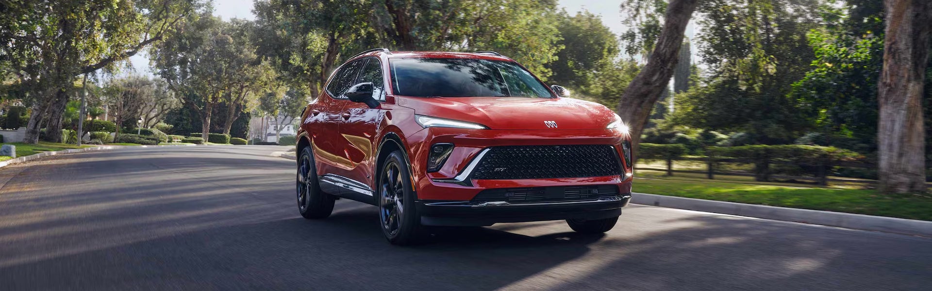 Red Buick Envision driving through a leafy suburban neighborhood